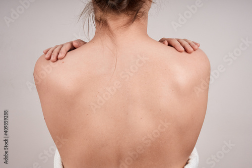 Faceless woman back view topless, hands on shoulders, isolate on gray background.