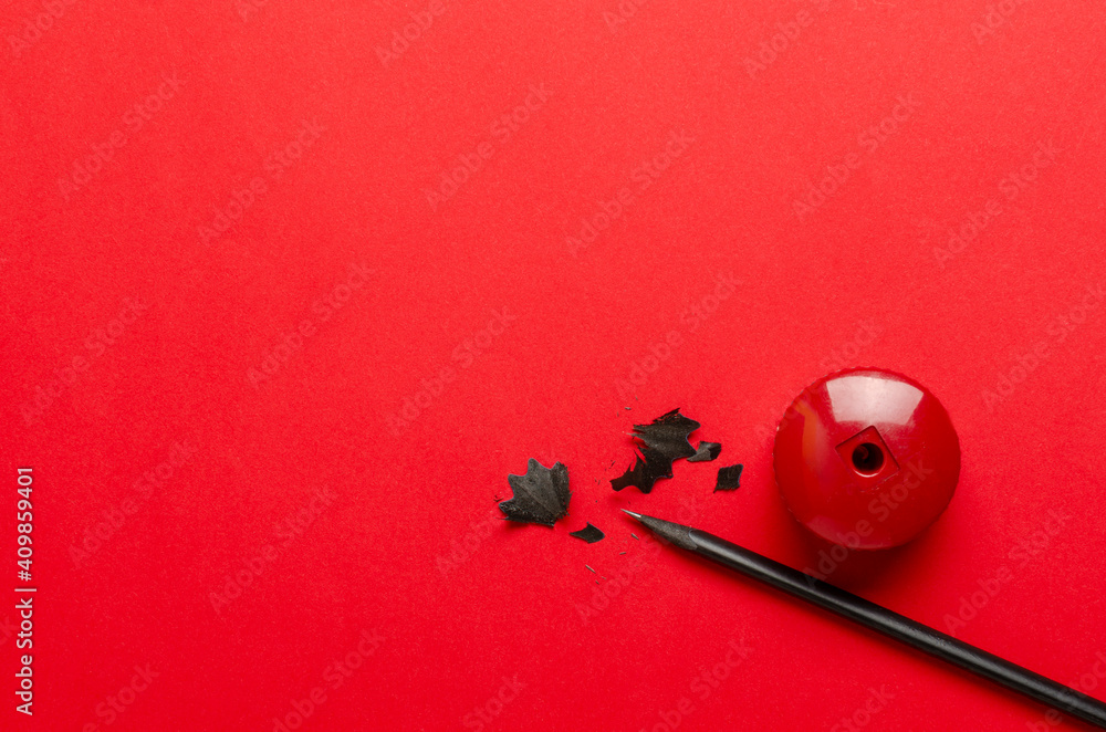 Top view of black pensil, red pensil sharpener, shavings on the bright red surface.Empty space Top view of black pensil, red pensil sharpener, shavings on the bright red surface.Empty space