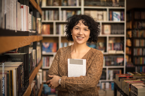 Portrait of smiling in library holding a book. Looking at camera.