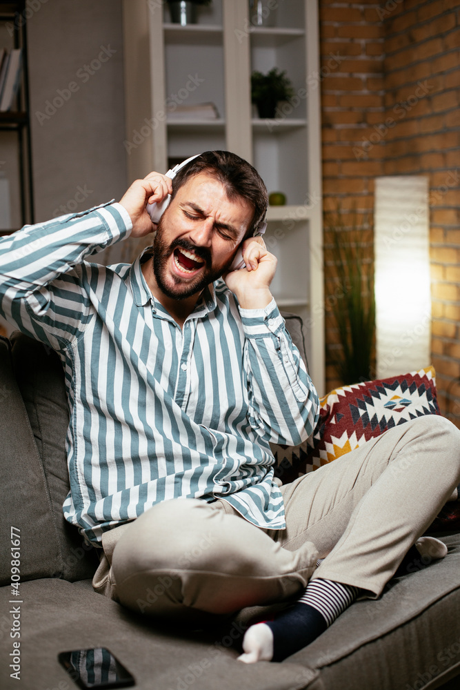 Obraz premium Young man with headphones resting on sofa. Happy man singing and listening the music.