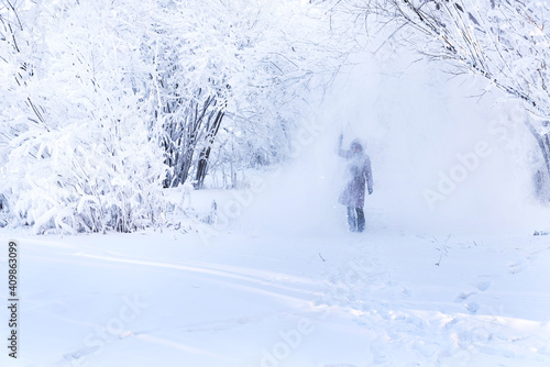 Woman standing under falling snow in winter forest. Carefree woman enjoying snow and winter time, playing with snow. Winter leisure concept.