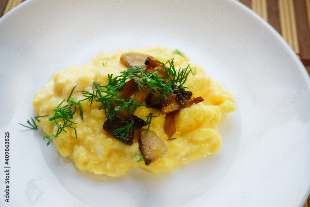 Close-up of appetizing scrambled eggs with mushrooms and dill on a white plate. Healthy protein breakfast. Home cooking concept. Close-up of appetizing scrambled eggs with mushrooms and dill on a white plate. Healthy protein breakfast. Home cooking concept.
