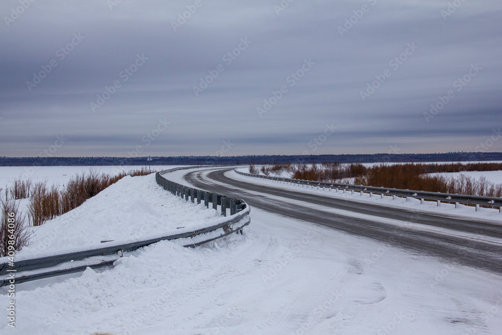 Obraz premium Winter track in the North. Two-lane track with bumpers, fences, snow and ice.