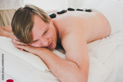 A young man is happy and relaxed with a hot stone therapy in the spa.