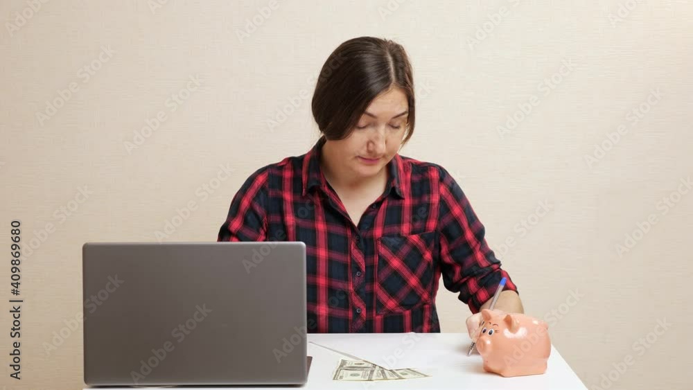 Serious young woman in checkered shirt sits at table near laptop planning family budget closeup Serious young woman in checkered shirt sits at table near laptop planning family budget closeup