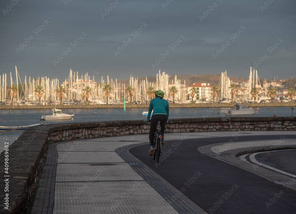 Obraz premium Una mujer andando en bici por una paseo al lado de la costa con Hendaya de fondo. 