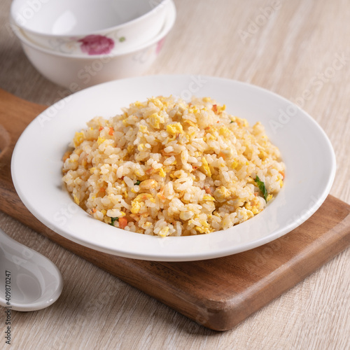 Chinese fried rice in white plate on bright wooden table background.