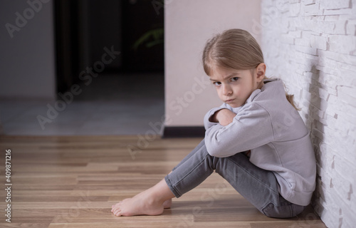 Sad,angry and depressed punished little girl child sitting on the floor near the wall at home. Stop bullying .