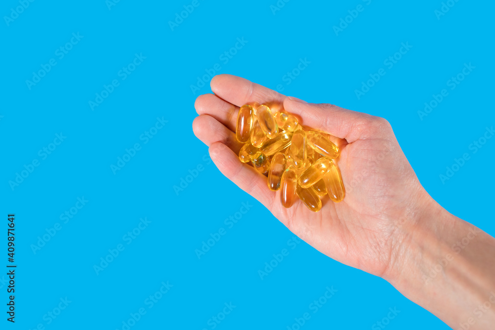 Capsules of fish oil in the palm of a person on a blue background. A physician's recommendation for using fish oil as a dietary supplement to improve cardiovascular health. Free space for text Capsules of fish oil in the palm of a person on a blue background. A physician's recommendation for using fish oil as a dietary supplement to improve cardiovascular health. Free space for text