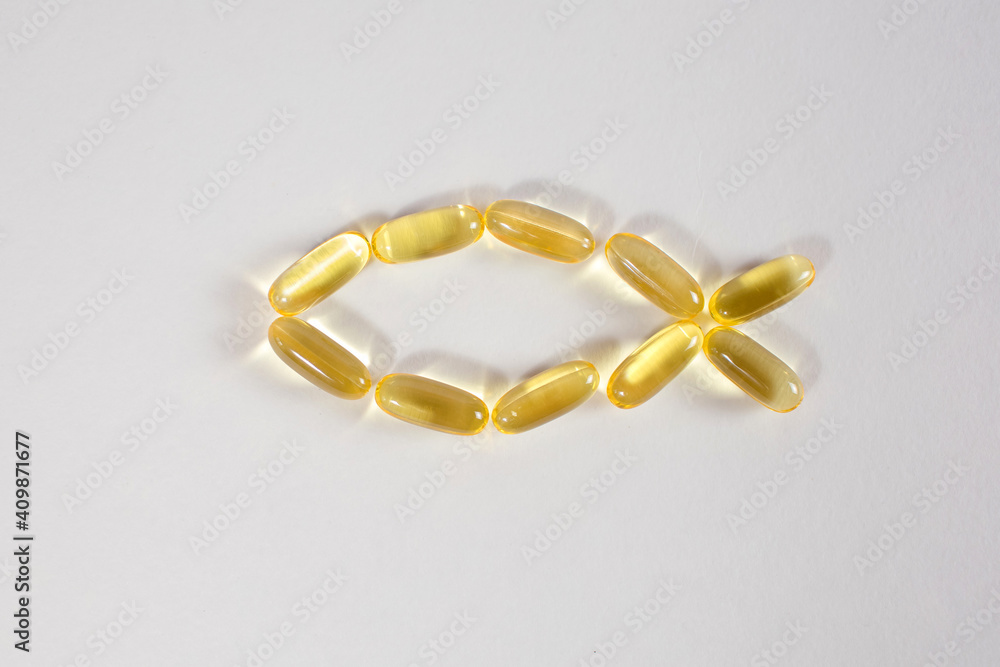 Fish oil capsules in the shape of a fish on a white background. Food supplement for human health that improves the functioning of the cardiovascular system. Top view of bright transparent capsules