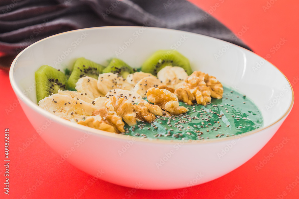 spirulina smoothie bowl with banana, walnuts, kiwi and chia seeds on red background spirulina smoothie bowl with banana, walnuts, kiwi and chia seeds on red background