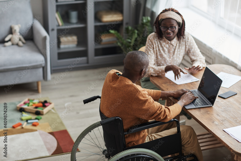 © Seventyfour - High angle portrait of African-American man using wheelchair working from home with wife, copy space © Seventyfour - High angle portrait of African-American man using wheelchair working from home with wife, copy space