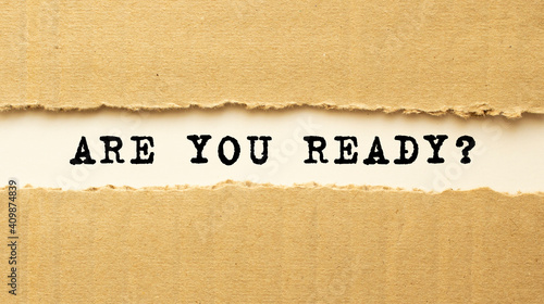 Text ARE YOU READY appearing behind torn brown paper. Top view.