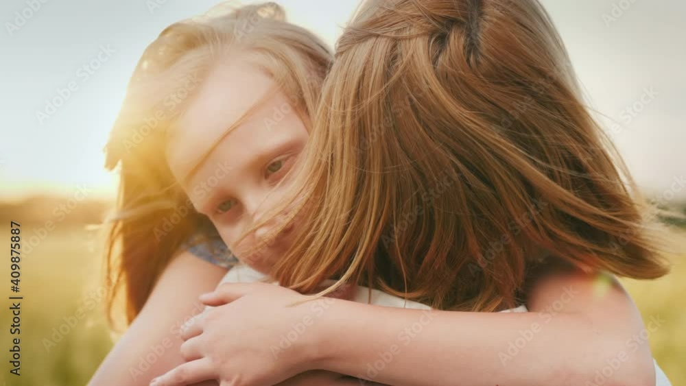 Mom hugs her daughter at sunset, wind plays with their hair