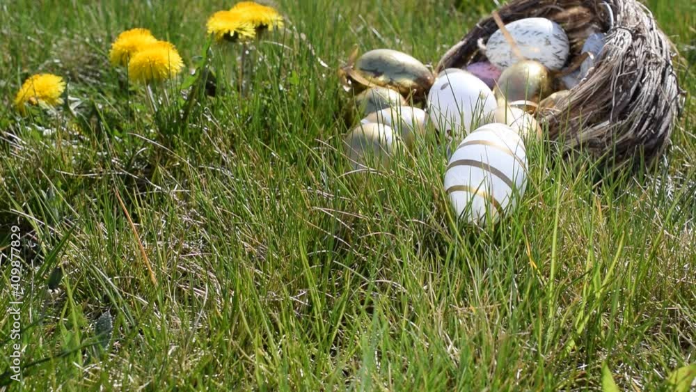 Easter basket eggs. Golden egg with yellow spring flowers in celebration basket on green grass background. Traditional decoration in sun light Easter basket eggs. Golden egg with yellow spring flowers in celebration basket on green grass background. Traditional decoration in sun light