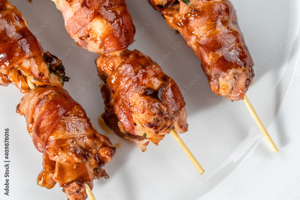Grilled bacon-wrapped chicken tenders are laid out on a white plate. Strung on wooden skewers-2.