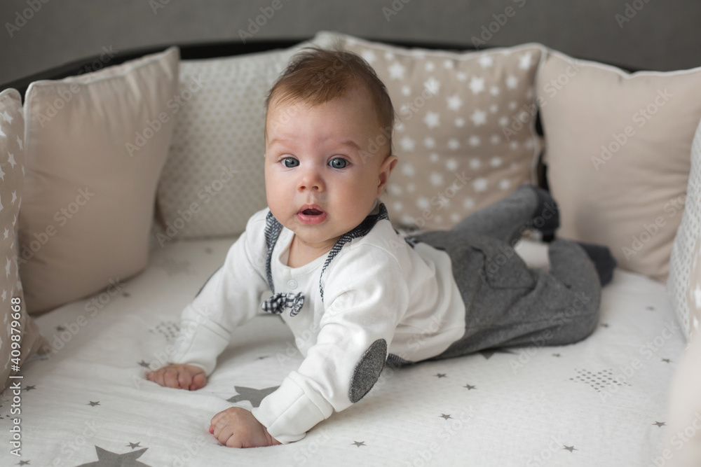 A cute little baby boy is surprised lying on the bed. Closeup portrait of newborn baby looking at camera A cute little baby boy is surprised lying on the bed. Closeup portrait of newborn baby looking at camera