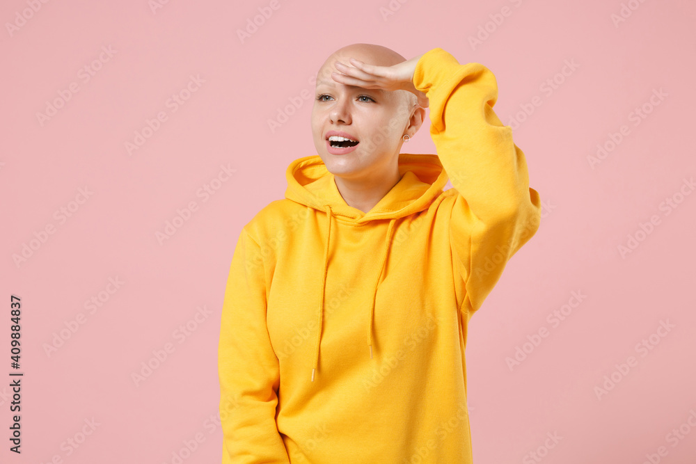 Young bald smiling caucasian friendly successful happy cheerful happy woman 20s without hair wearing yellow casual sweatshirt shirt look far away distance isolated on pink background studio portrait. Young bald smiling caucasian friendly successful happy cheerful happy woman 20s without hair wearing yellow casual sweatshirt shirt look far away distance isolated on pink background studio portrait.