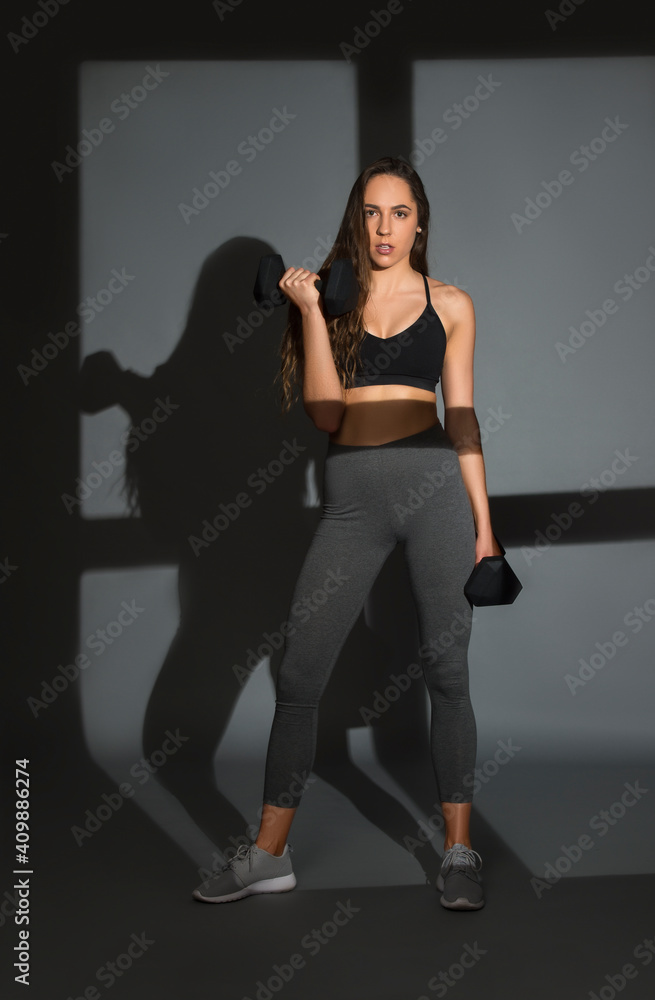 Young  female doing fitness with dumbbels on grey background. Workout online concept. Vintage color filter