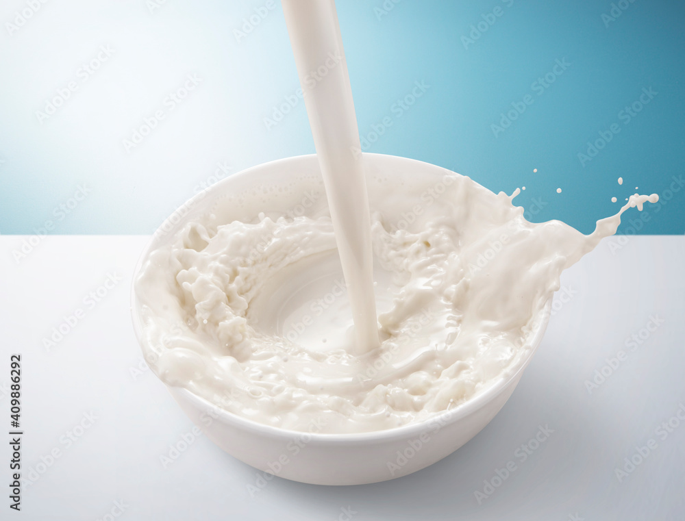 Fresh milk pouring in bowl with splash. isolated on blue and white background. - obrazy, fototapety, plakaty 