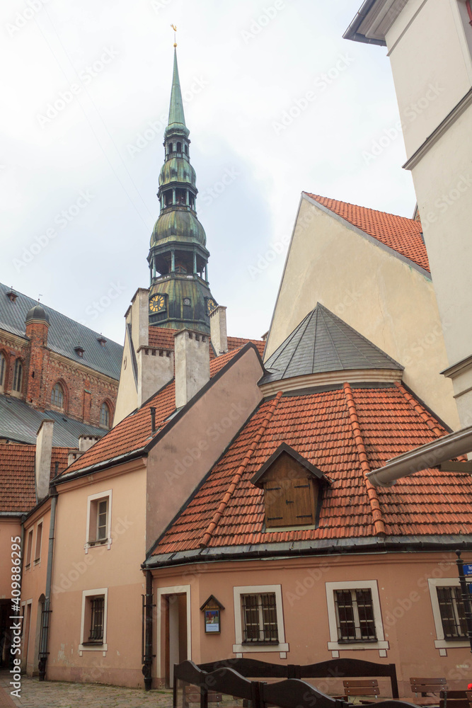 Obraz premium Famous view on latvian highest unique medieval and gothic architecture church tower with clock and the roofs of old houses on street in the center of capital old city Riga, Latvia, the Baltic region