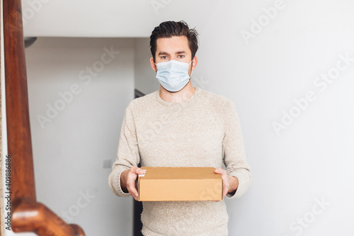 A delivery guy in medical mask holding a cardboard box and looking at the camera 