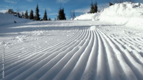 Skipiste mit Spuren einer Pistenraupe an einem Sonnentag mit blauem Himmel