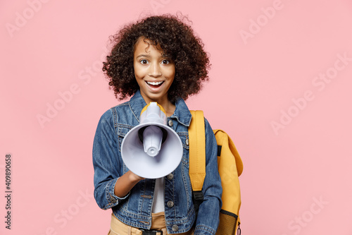 Smiling leader little african american kid school girl 12-13 years old in casual denim clothes with backpack scream in megaphone isolated on pastel pink background studio Childhood education concept.