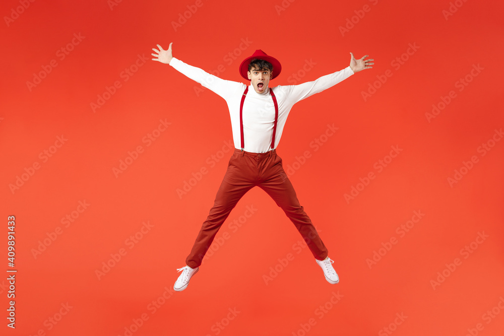 Full length of young spanish latinos overjoyed weird shocked fun happy man 20s in hat white shirt trousers, suspenders jump high with outstretched hands legs isolated on red background studio portrait