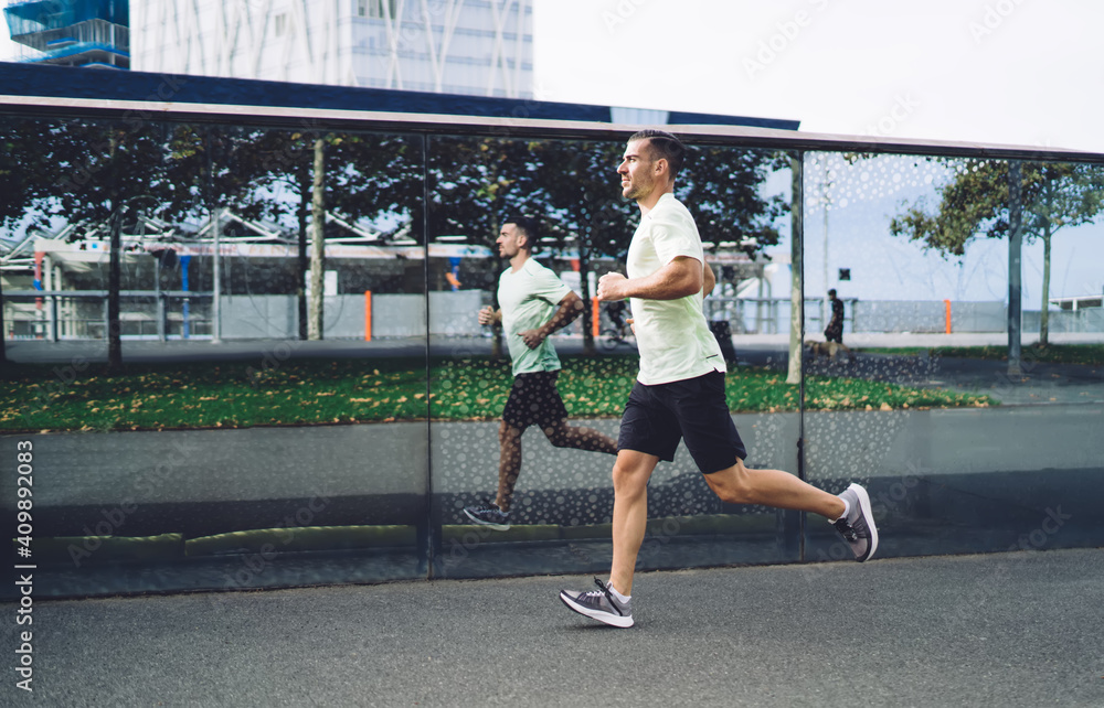 Side view of determined male athlete getting ready to marathon have cardio morning training at city urbanity, motivated man in sportswear jogging with speed around street keeping healthy lifestyle
