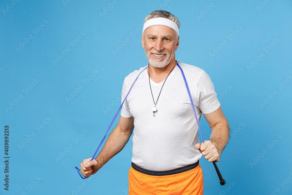 Elderly gray-haired sportsman trainer instructor smiling coach man 50s wearing sportswear white t-shirt whistle hold skipping rope isolated on blue background studio portrait. Fitness sport concept