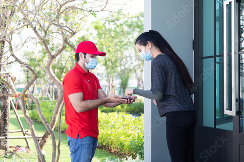Signing signature on smart phone device to get a package. woman receiving package from delivery man in red uniform . Protection face mask quarantine pandemic coronavirus virus 2019-ncov