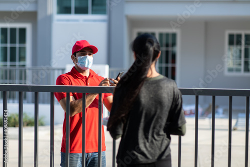 Signing signature on smart phone device to get a package. woman receiving package from delivery man in red uniform . Protection face mask quarantine pandemic coronavirus virus 2019-ncov