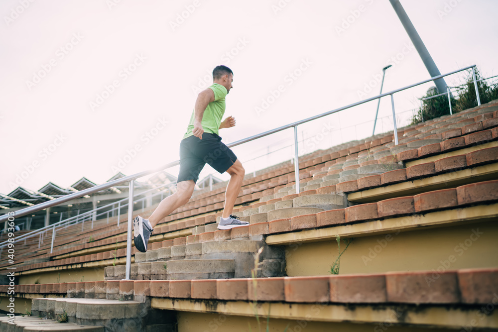 Strong energetic male runner in tracksuit enjoying active and healthy lifestyle have morning cardio workout for keeping perfect body shape, motivated sportsman jogging with speed at stadium stairs