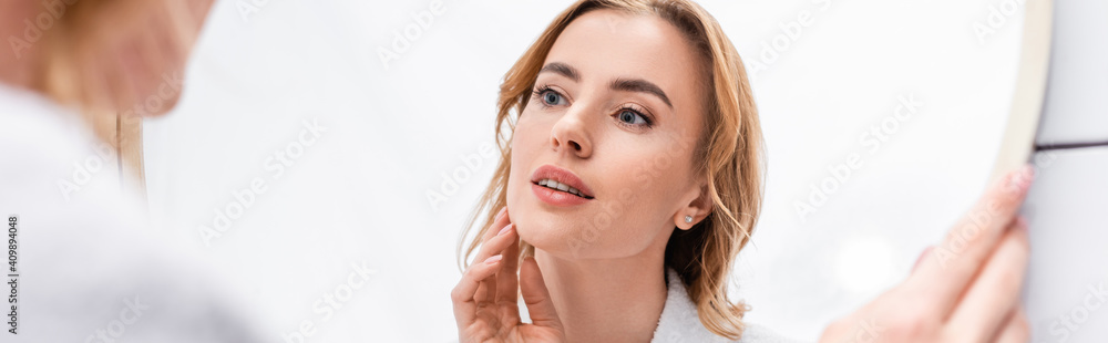woman looking at mirror and touching face in bathroom, banner
