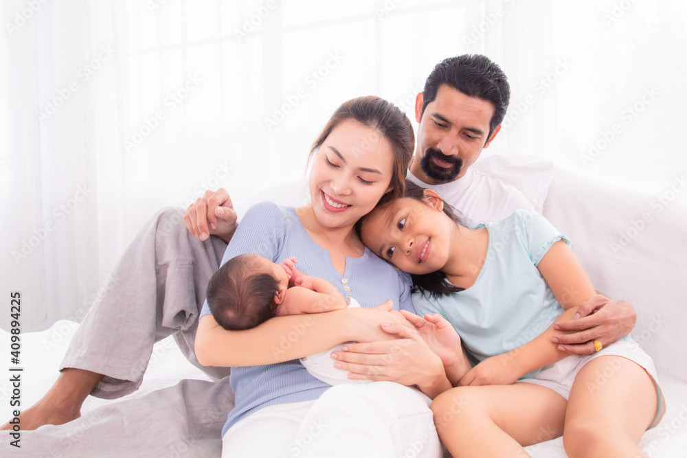 Proudly Asian man hug wife and 2 kids with love, care, protection, adorable daughter lie down on father's bosom or chest looking newborn brother in mother hand play infant feet, happy family concept