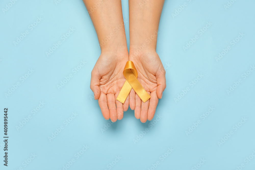 Obraz premium Hands with golden ribbon on color background. Childhood cancer awareness concept