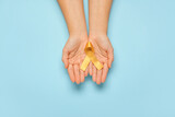 Hands with golden ribbon on color background. Childhood cancer awareness concept