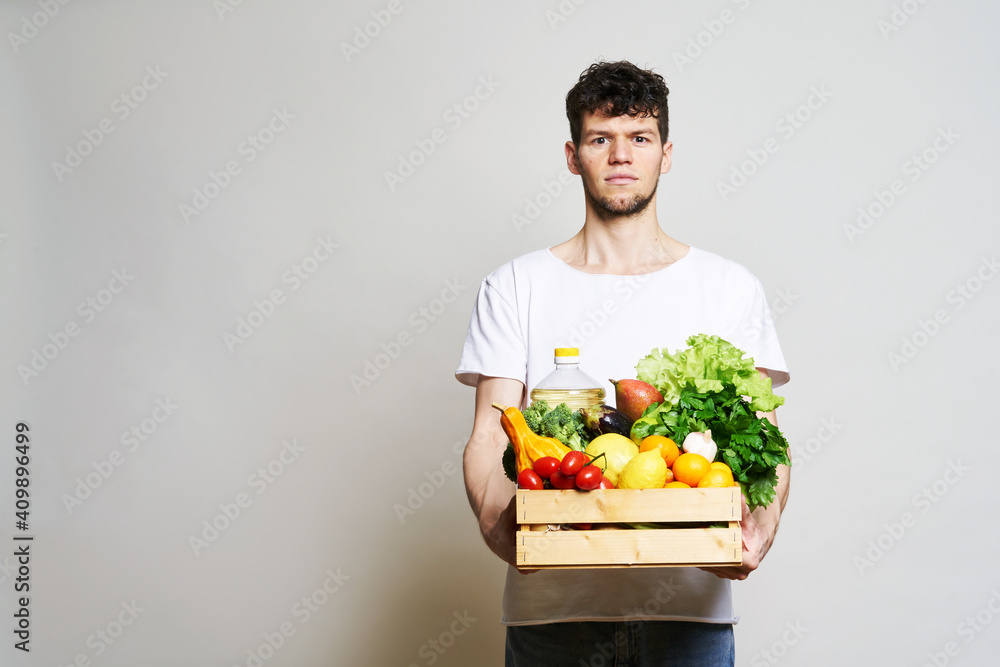 online shopping concept. A man in T-shirt holds a box of fresh food in his hands. Food delivery from the supermarket, from farmers. Delivery during quarantine online shopping concept. A man in T-shirt holds a box of fresh food in his hands. Food delivery from the supermarket, from farmers. Delivery during quarantine
