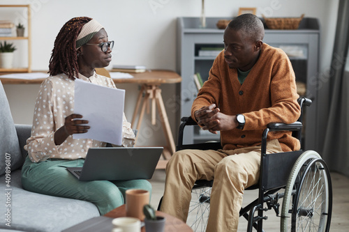 Portrait of African-American couple with handicapped man using wheelchair working from home together in modern interior photo
