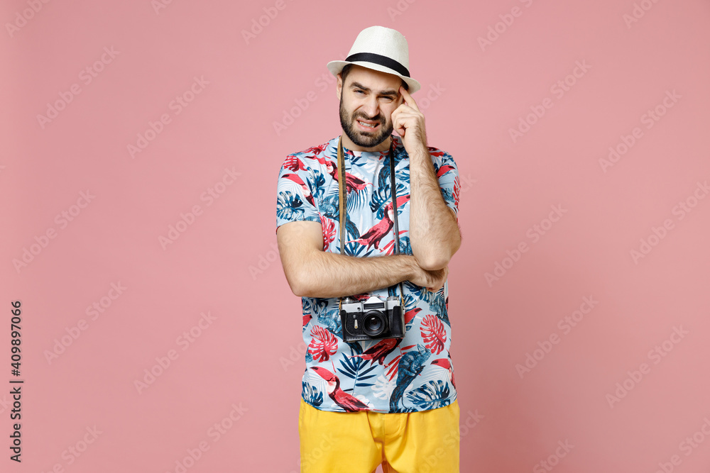 Puzzled worried young traveler tourist man in summer casual clothes hat with photo camera put hand on head isolated on pink background. Passenger traveling on weekends. Air flight journey concept.