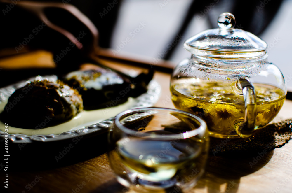 Tea pot and cup clear color natural herbal flower, chamomile, Japanese and Chinese green tea, rose. Bakery and pastries background blurred during morning time Tea pot and cup clear color natural herbal flower, chamomile, Japanese and Chinese green tea, rose. Bakery and pastries background blurred during morning time