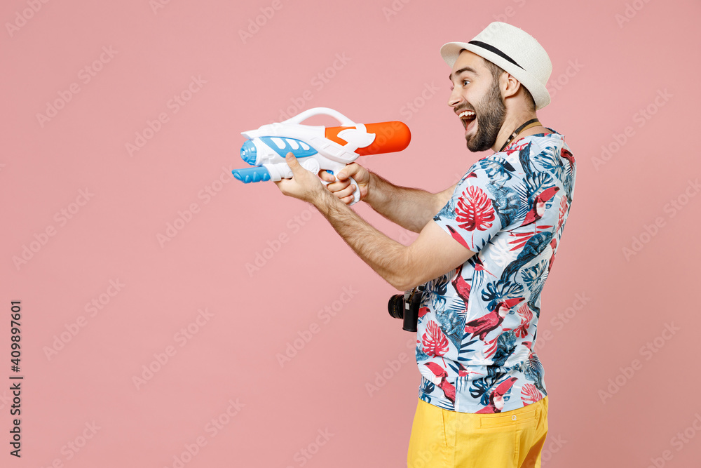 Excited young traveler tourist man in summer basic clothes hat photo camera hold toy water gun isolated on pink background studio portrait. Passenger traveling on weekend. Air flight journey concept. Excited young traveler tourist man in summer basic clothes hat photo camera hold toy water gun isolated on pink background studio portrait. Passenger traveling on weekend. Air flight journey concept.