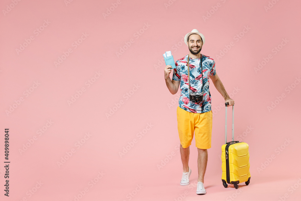 Full length of cheerful young traveler tourist man in summer clothes hat hold suitcase passport tickets isolated on pink background studio. Passenger traveling on weekends. Air flight journey concept. Full length of cheerful young traveler tourist man in summer clothes hat hold suitcase passport tickets isolated on pink background studio. Passenger traveling on weekends. Air flight journey concept.