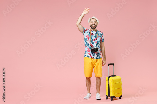 Tablou pe pânză Full length of excited traveler tourist man in summer clothes hat waving greeting with hand as notices someone isolated on pink background