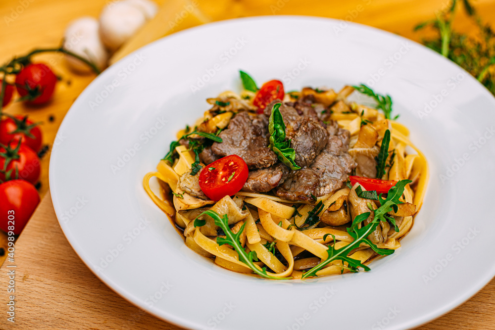 Fetuccini with fried meat and tomatoes on a decorated table