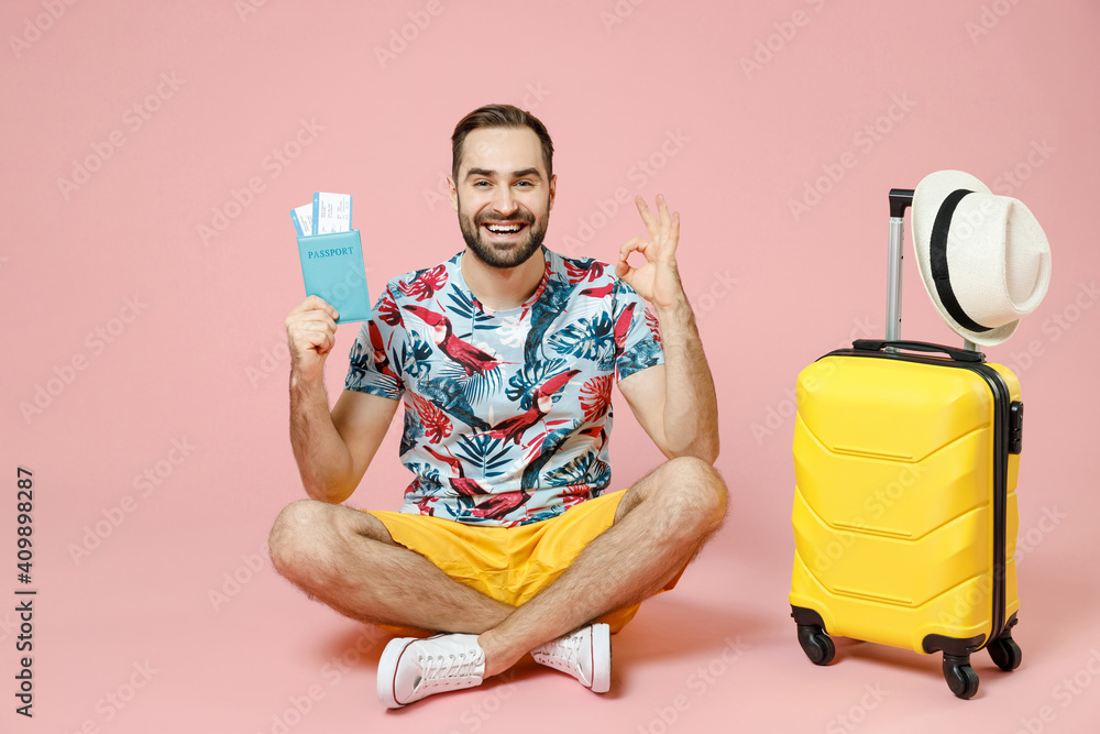 Full length cheerful traveler tourist man sit on floor near suitcase hold passport tickets showing ok okay gesture isolated on pink background. Passenger travel on weekend. Air flight journey concept. Full length cheerful traveler tourist man sit on floor near suitcase hold passport tickets showing ok okay gesture isolated on pink background. Passenger travel on weekend. Air flight journey concept.