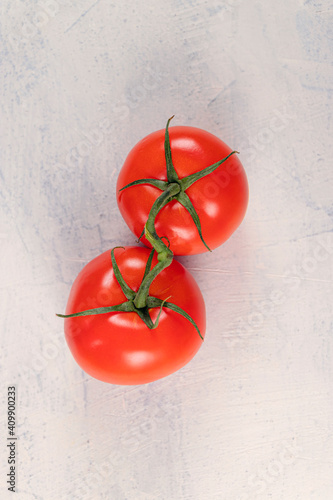 Two red tomatoes on a green branch on a white stone background. Ripe, fresh, juicy tomatoes. Copy space