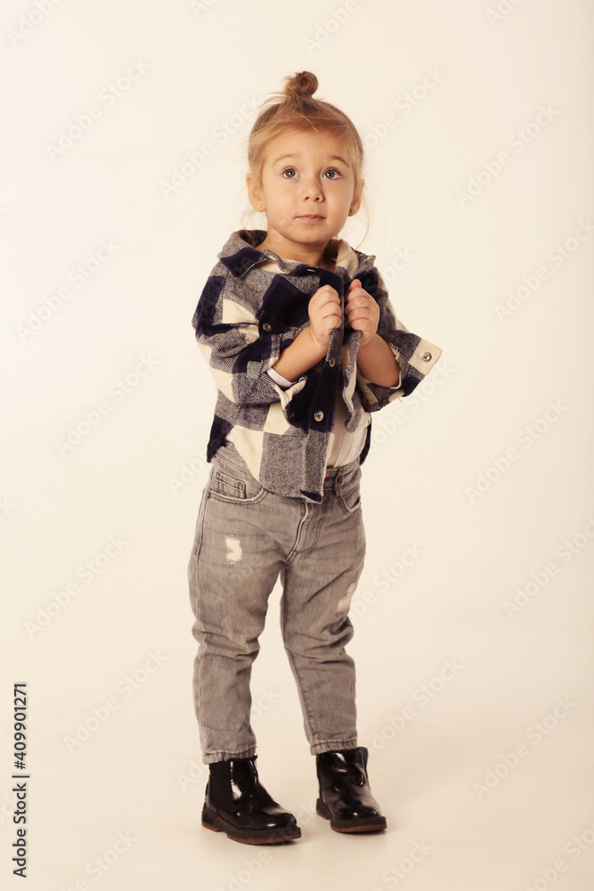 cute little blond baby girl in black boots, jeans, checkered shirt with copy space cute little blond baby girl in black boots, jeans, checkered shirt with copy space