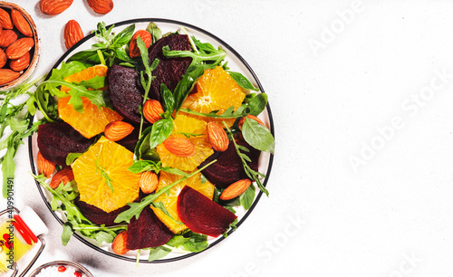 Beetroot Salad with Orange, arugula and almonds nut on white background. Vegan healthy summer food. Top view. Copy space
